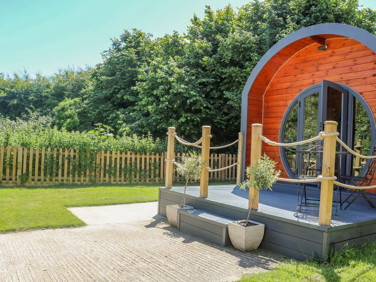 Filbert Pod with its curved wooden front, small raised porch and grass beside a picket fence