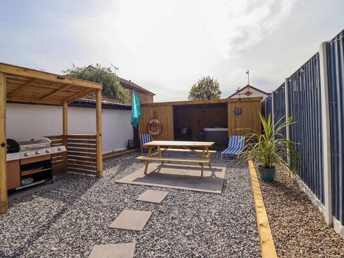 Fishermans Cottage gravel garden with picnic bench, covered barbecue and hot tub in a timber shelter
