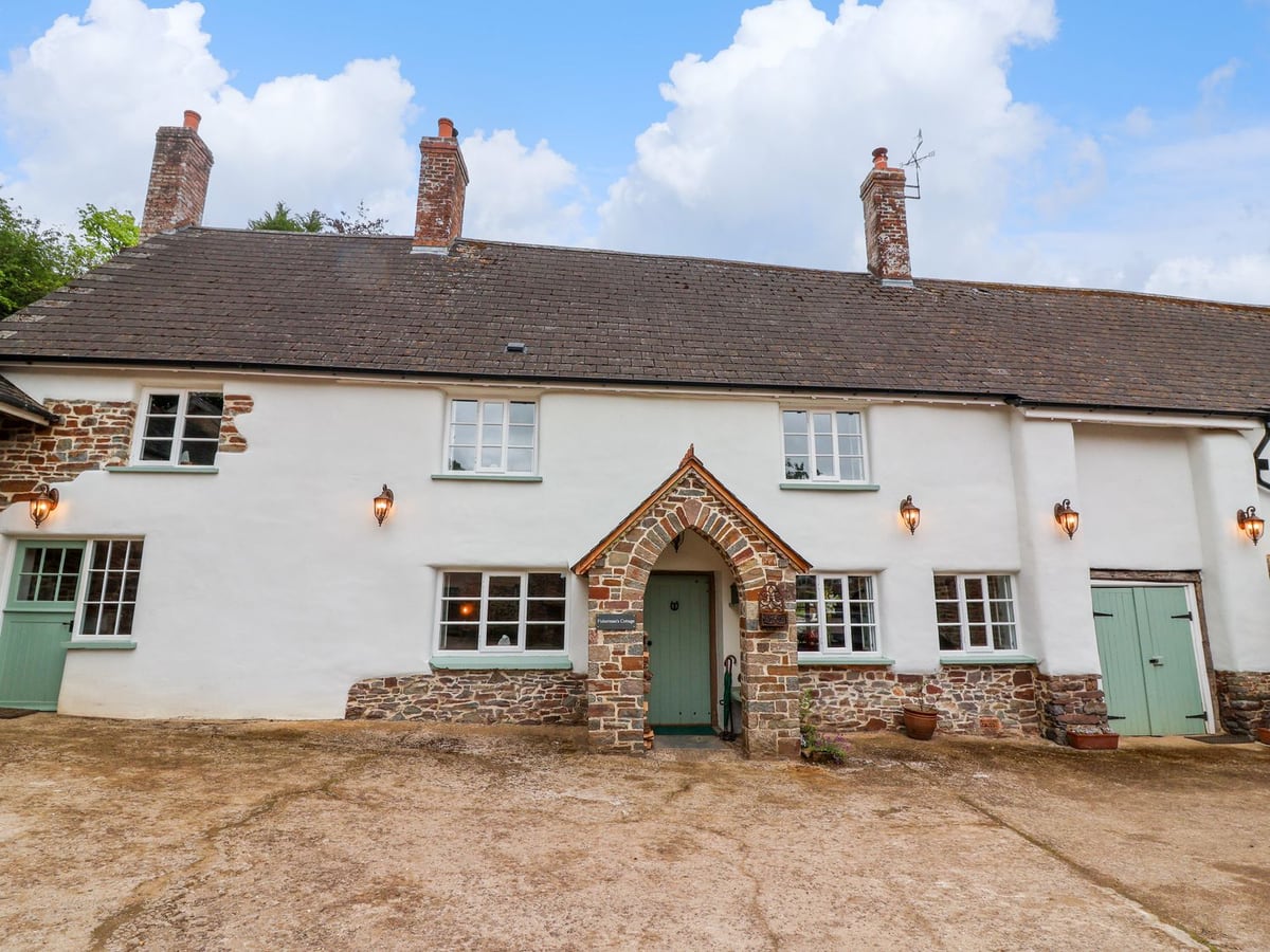 White cottage facade with green doors and a pointed stone porch at Fishermen's Cottage