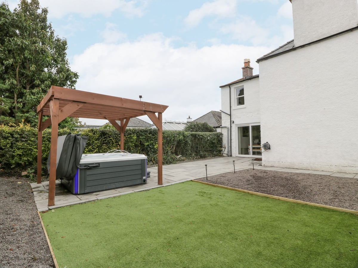 Fleetbank courtyard with a pergola-covered hot tub, artificial grass and paving beside the house