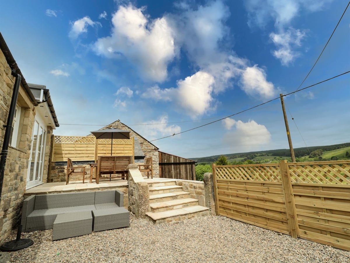 Gravel seating area and stone steps beside Fox View Cottage, with fields beyond the timber fence.