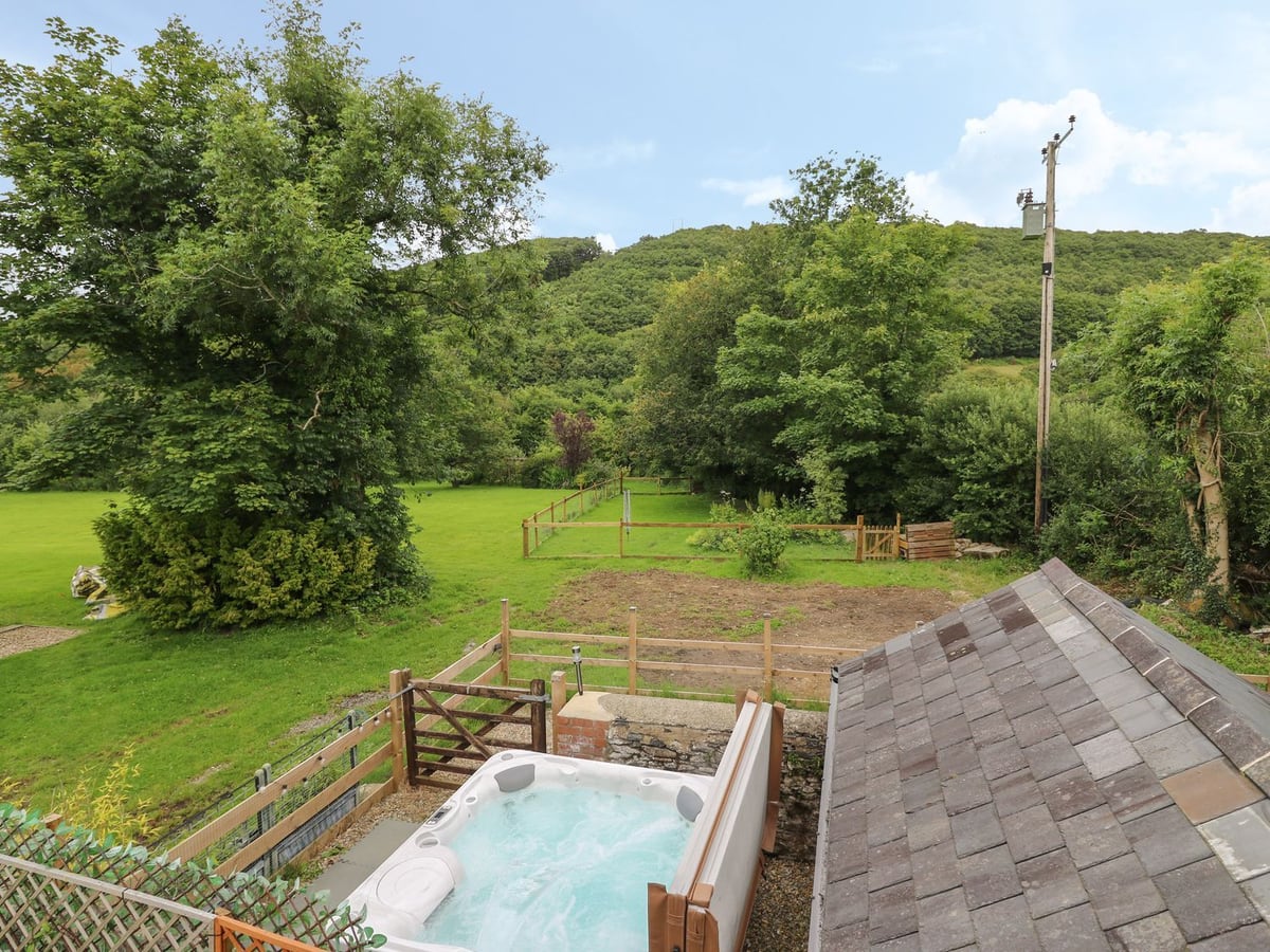 Hot tub in a fenced gravel area at Garden View, looking over lawn, a fenced paddock and wooded hills