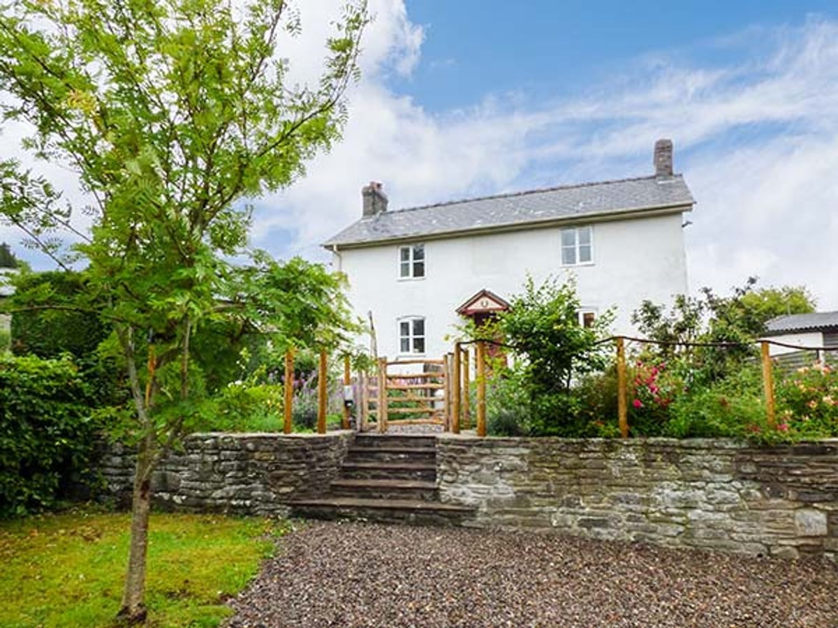 Gatehouse white cottage behind a wooden garden gate, stone steps, a low wall and trees