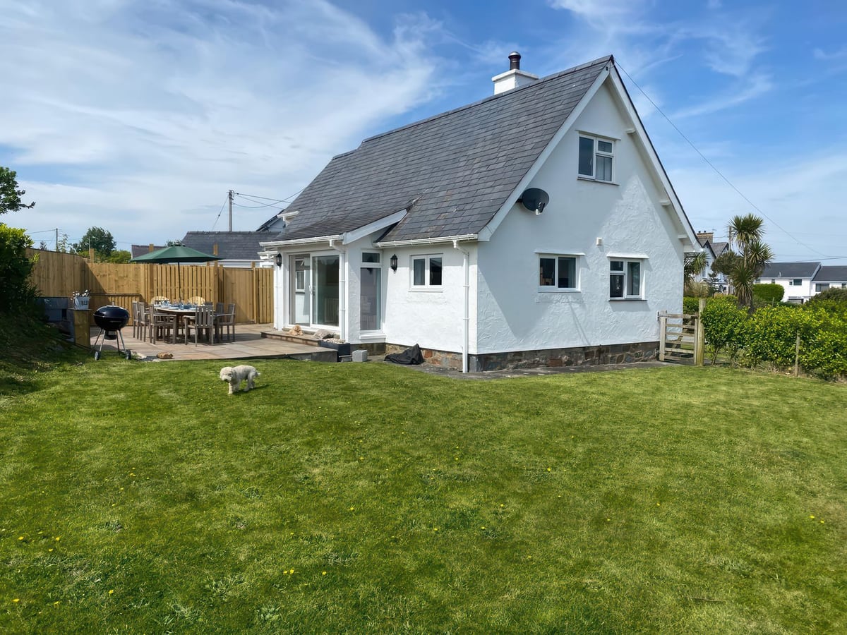 Gilfach white cottage with a large lawn, patio dining table under a parasol and a small dog on the grass