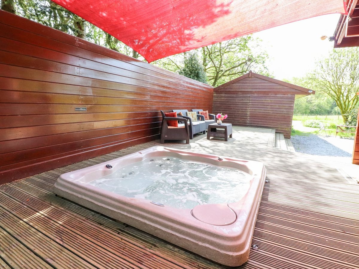 Sunken hot tub and outdoor seating beneath a red shade sail at Gisburn Forest Lodge
