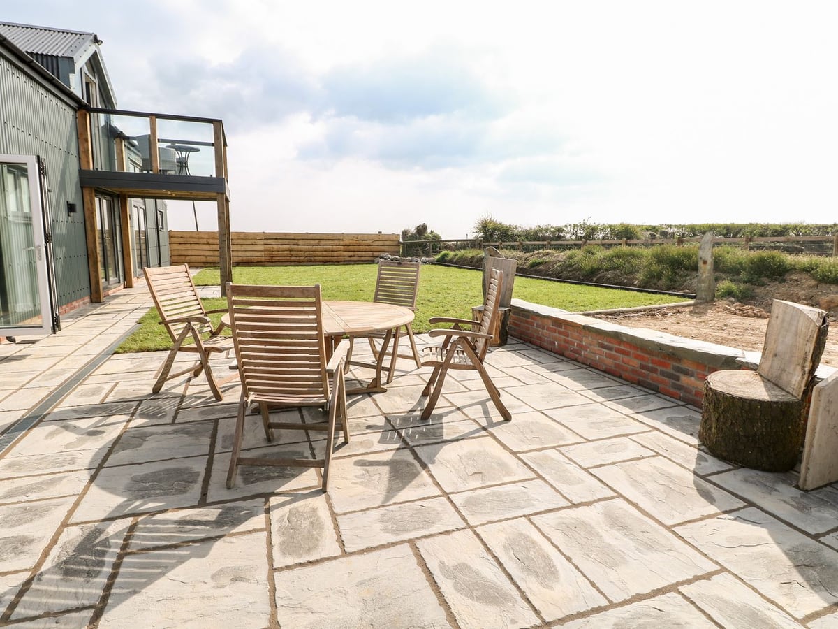 Glowty Brynbedw patio with wooden table and chairs beside a lawn, low brick wall and timber fencing