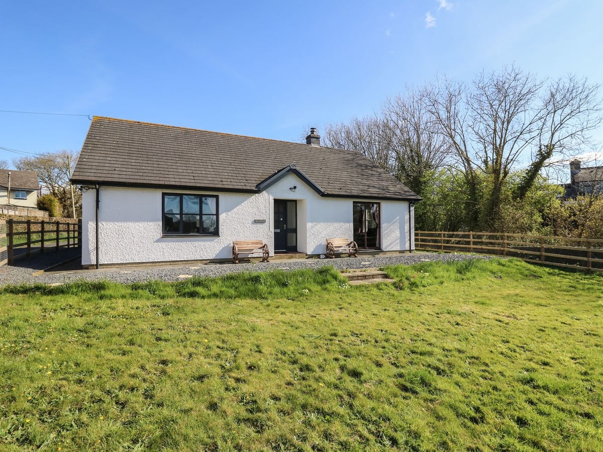 Glyn Cottage, a white single-storey cottage with two benches, a grassy lawn in front and a wooden fence
