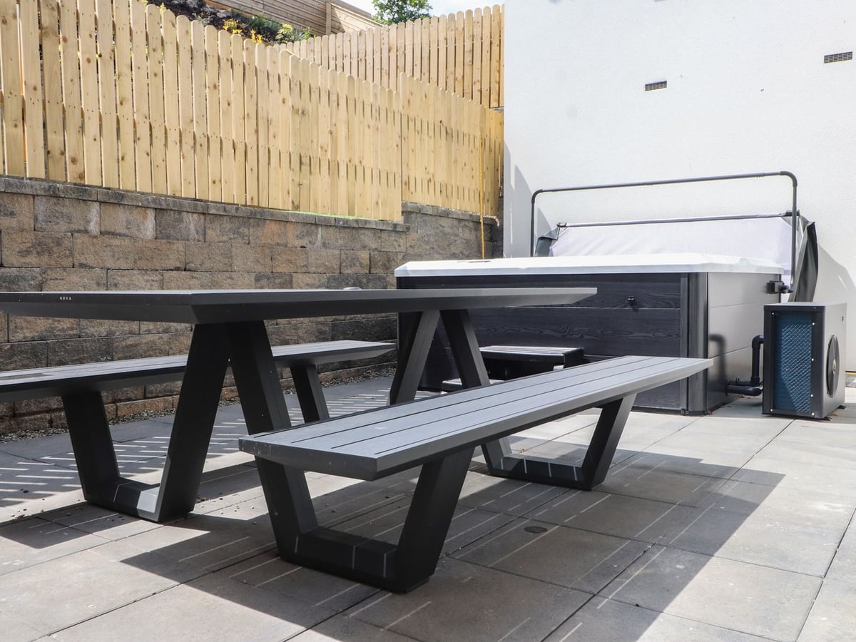 Golygfa Gele patio with picnic benches beside a hot tub, stone retaining wall and timber fence