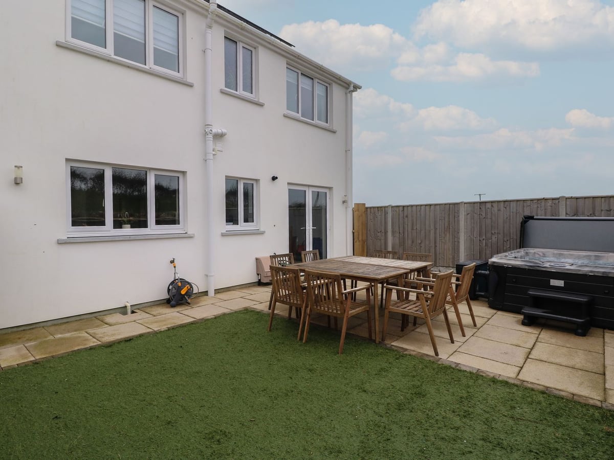 Rear of Golygfa Hafan with artificial lawn, patio dining table and hot tub beside a wooden fence