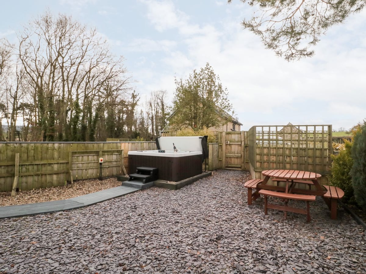 Hot tub and picnic table in the fenced gravel garden at Grange Cottages, with trees behind.