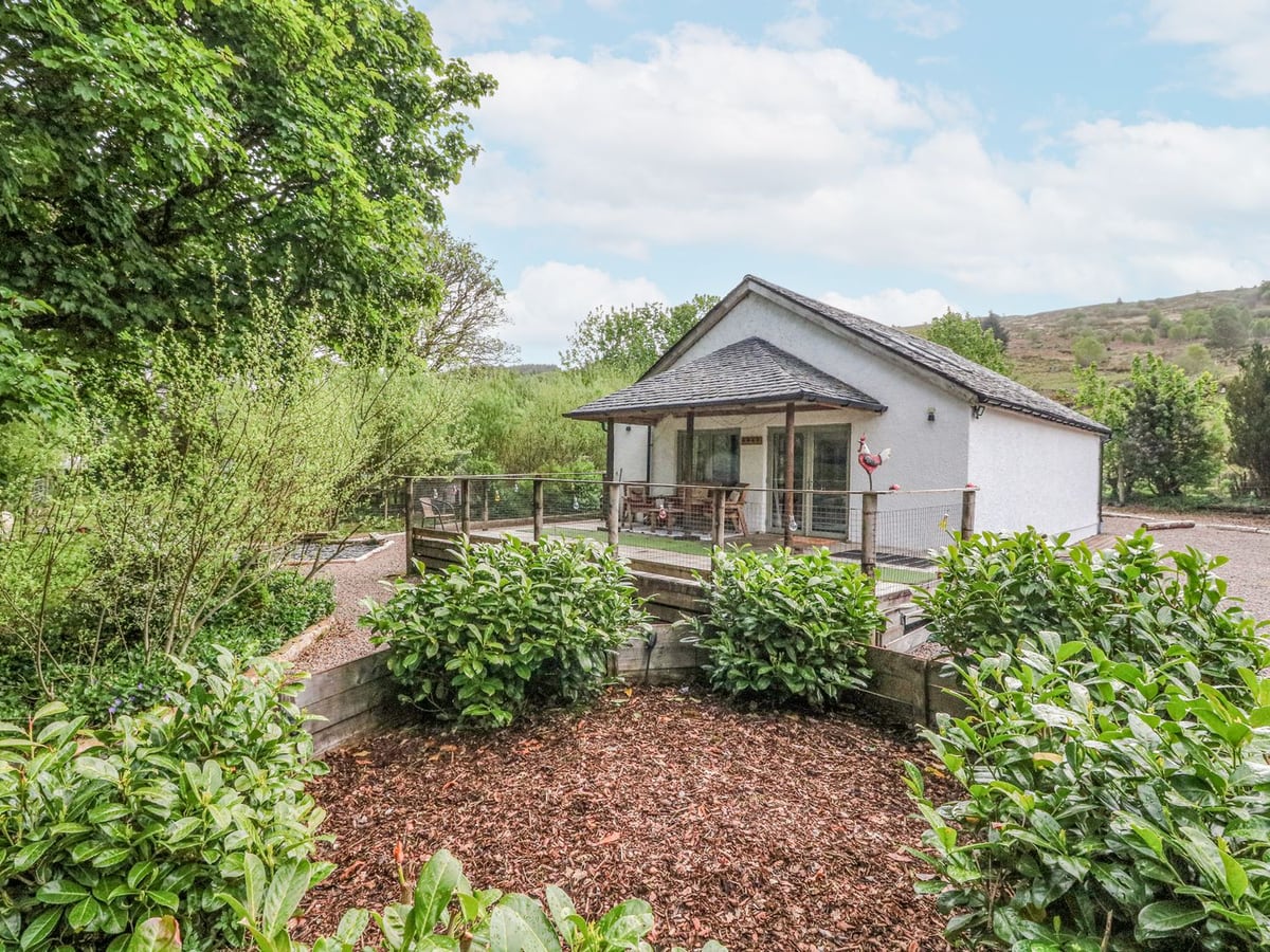 Grant Cottage with a covered timber veranda, garden shrubs and gravel paths around the house