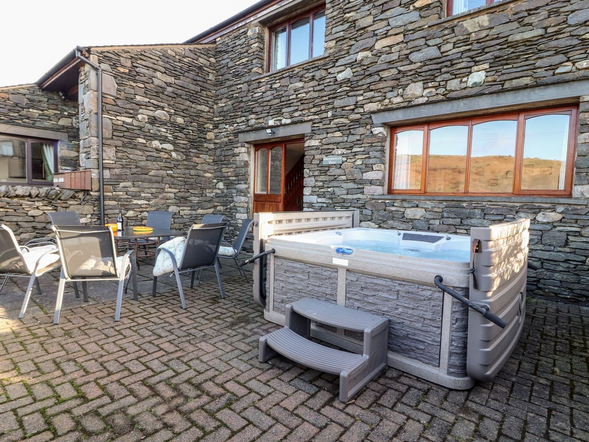 Green Hills Farm stone exterior with a hot tub and patio dining chairs beside the door