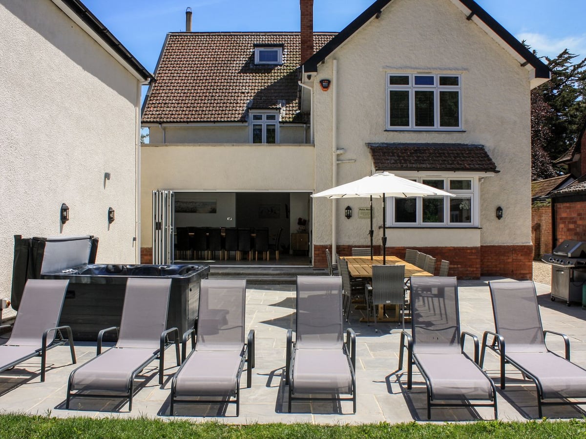Greenlawns patio with hot tub, dining table and loungers beside the house