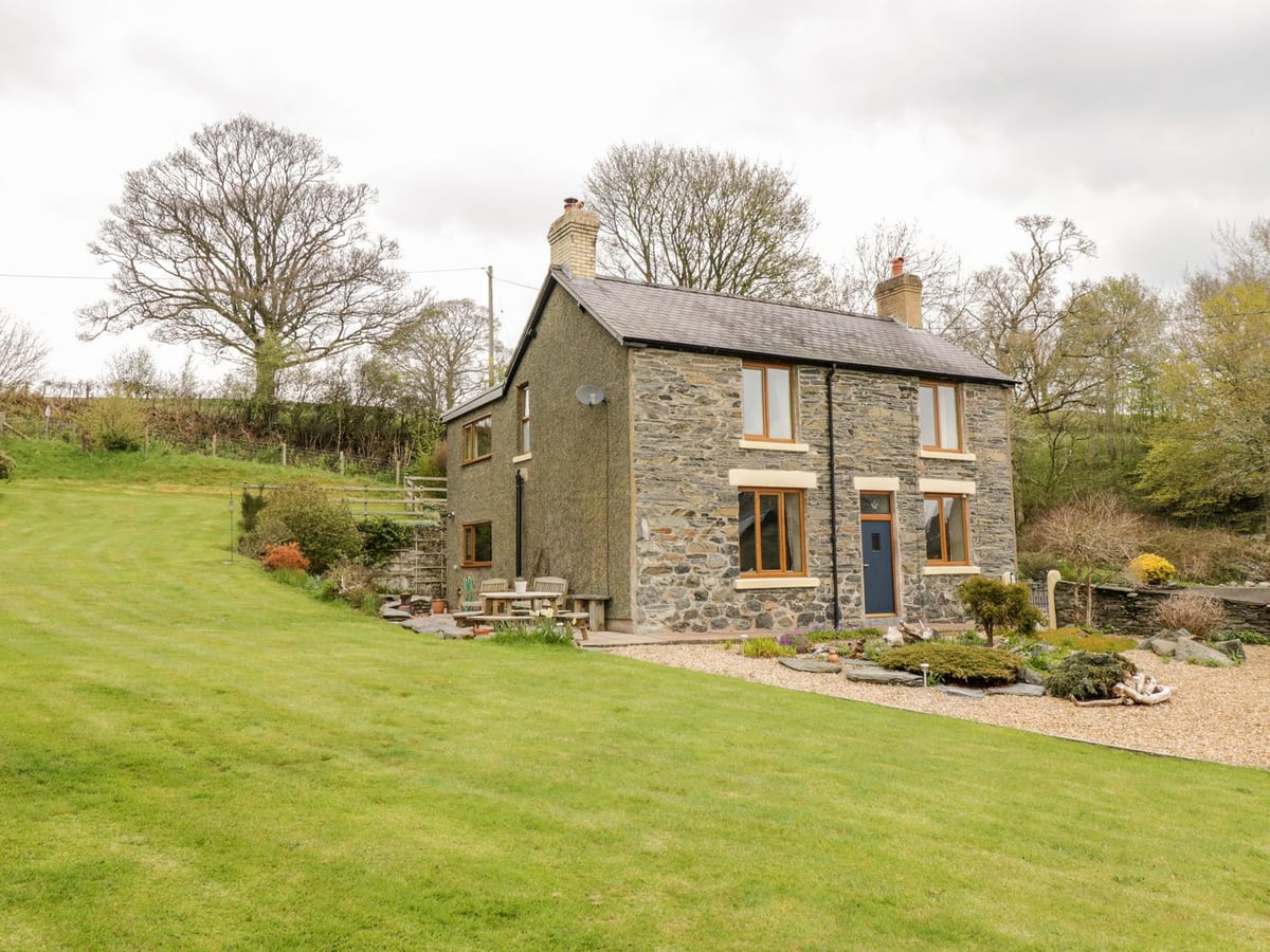 Groes Lwyd stone farmhouse with a sloping lawn, patio table and chairs and a gravel rockery