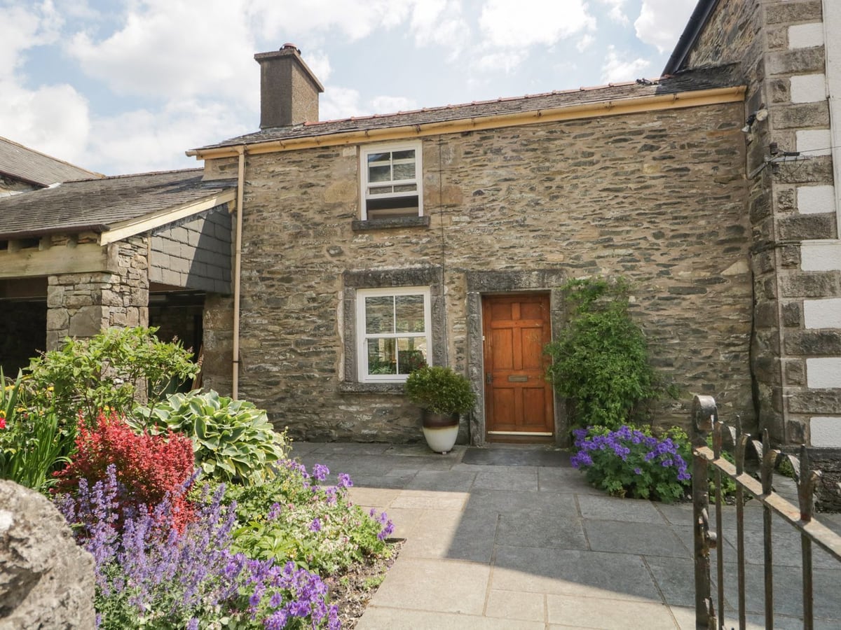 Grove House stone doorway and paved path framed by colourful flowers and an iron gate