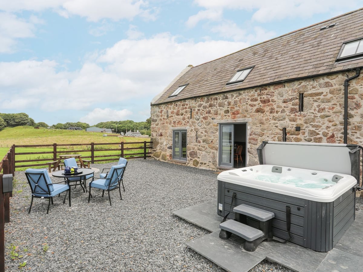 Gwel Y Fenai stone cottage patio with hot tub, blue chairs, and field views