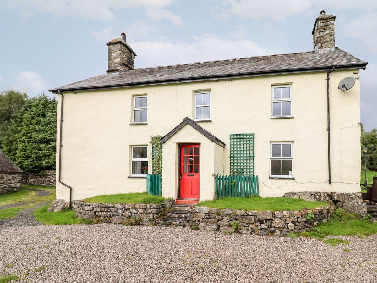 Gwengraig cream farmhouse with red front door, small lawn behind a low stone wall and a gravel drive