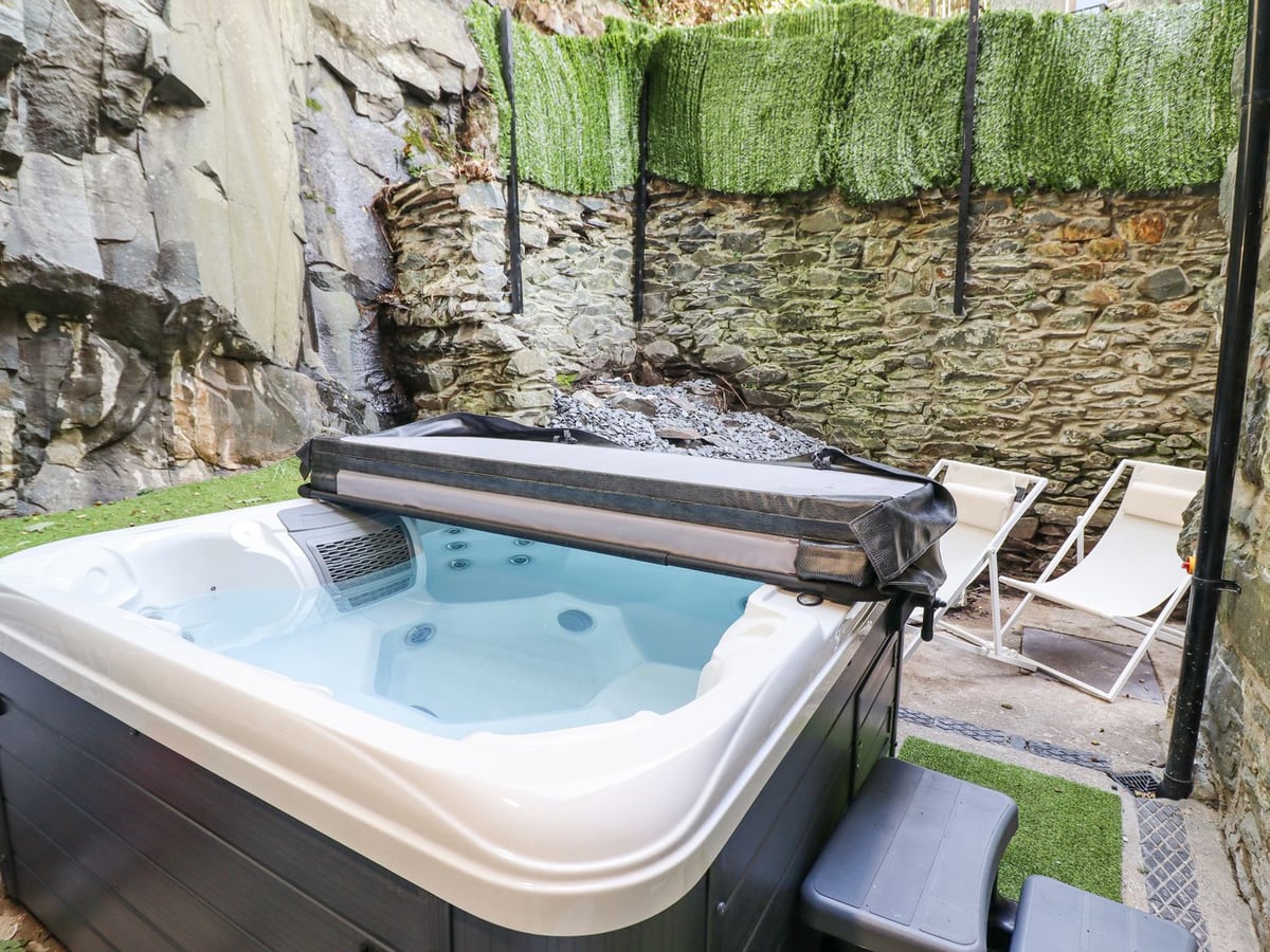 Gwynfa courtyard with hot tub, deckchairs, artificial grass strips and high stone and rock walls