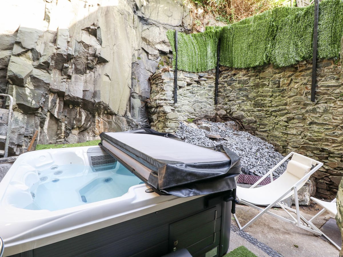 Gwynfa hot tub in a walled courtyard with rock face, lounger, and greenery