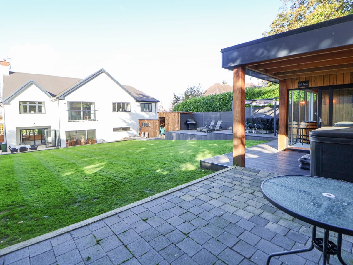 Hafan Y Mor rear lawn and paved patio, with the white house and a covered hot tub by the summerhouse