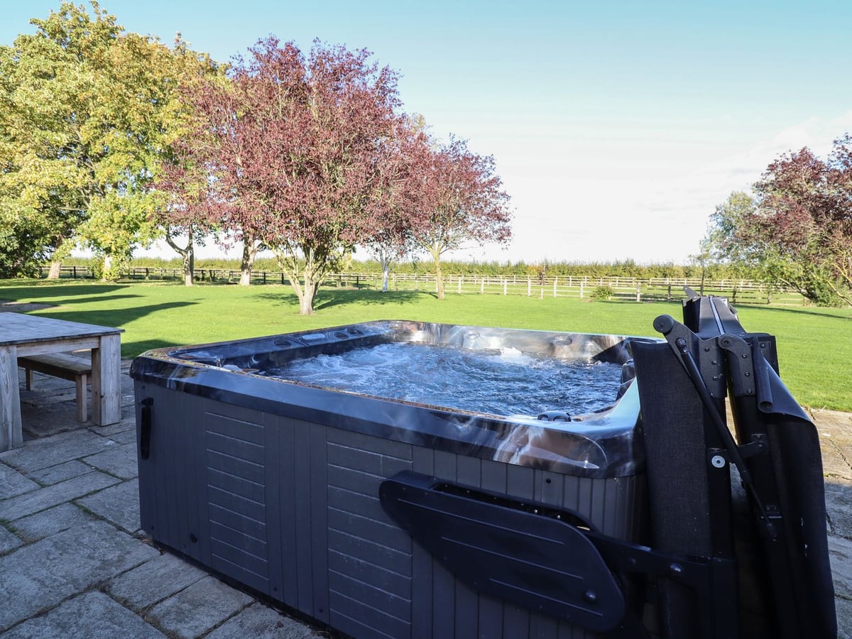 Open hot tub on Hall Farm's paved terrace with lawn and flowering trees beyond