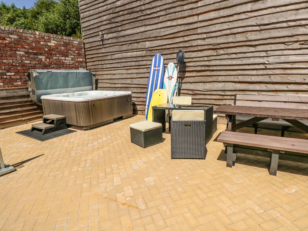 Paved rear patio at Harmon Vale with hot tub, rattan seats, picnic bench and timber and brick walls