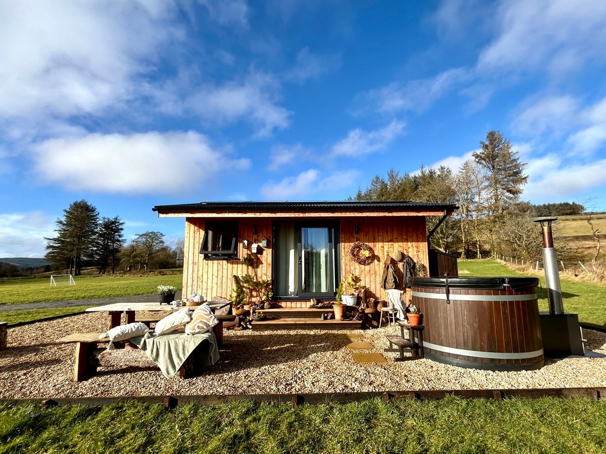 Harriet timber cabin with a gravel patio, table and benches and a round hot tub with its lid on