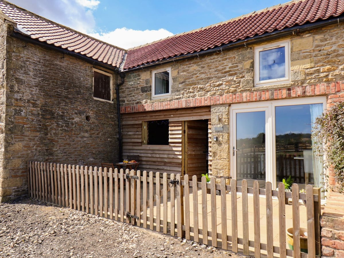 Stone exterior of Hawthorn Cottage with patio doors and a low timber fence around the patio