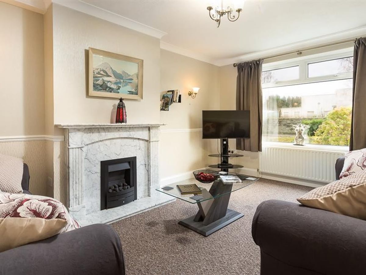 Heathfield living room with sofas, a marble fireplace and a glass table beside a large window