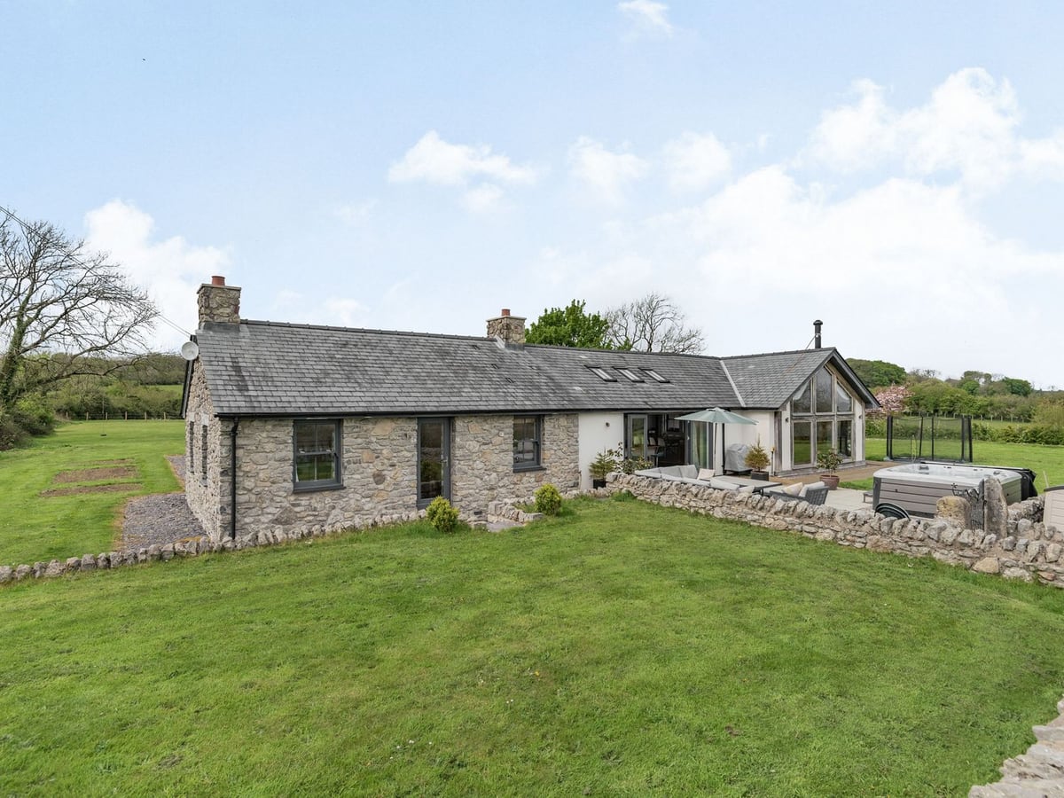 Hen Hafod stone house with a large lawn, low stone walls, a patio seating area and a hot tub