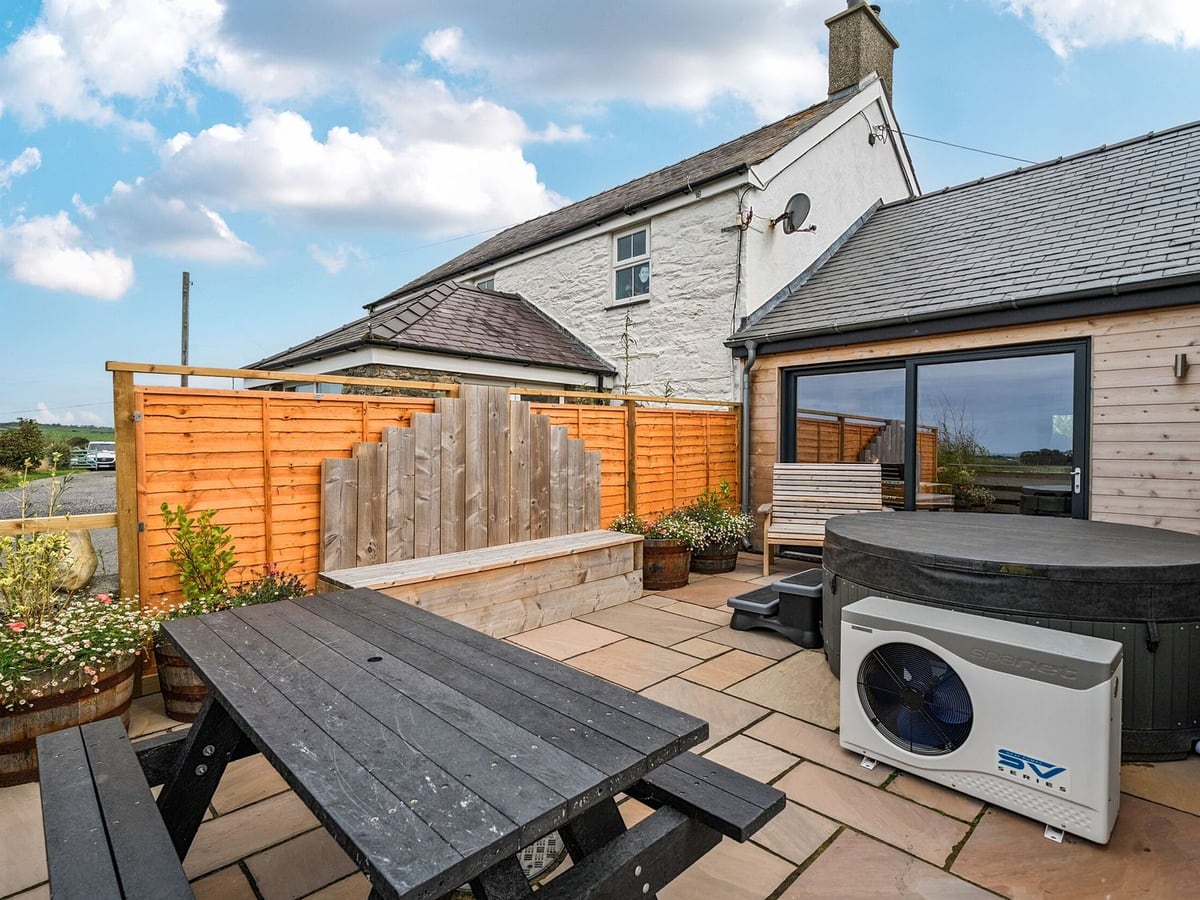 Hen Penmynydd paved patio with a picnic bench, planters, wood fencing and a hot tub with its lid on
