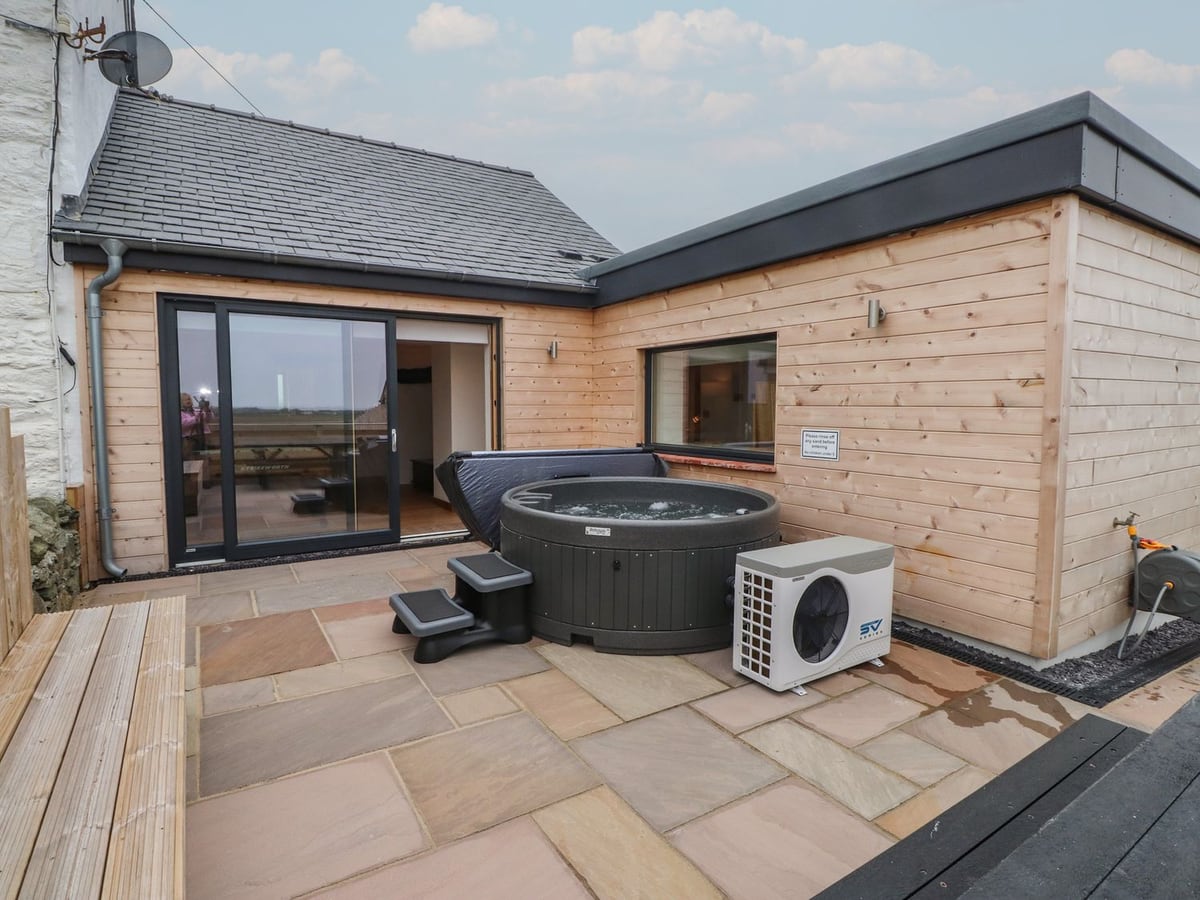 Hen Penmynydd rear patio with a round hot tub beside the timber-clad cottage extension
