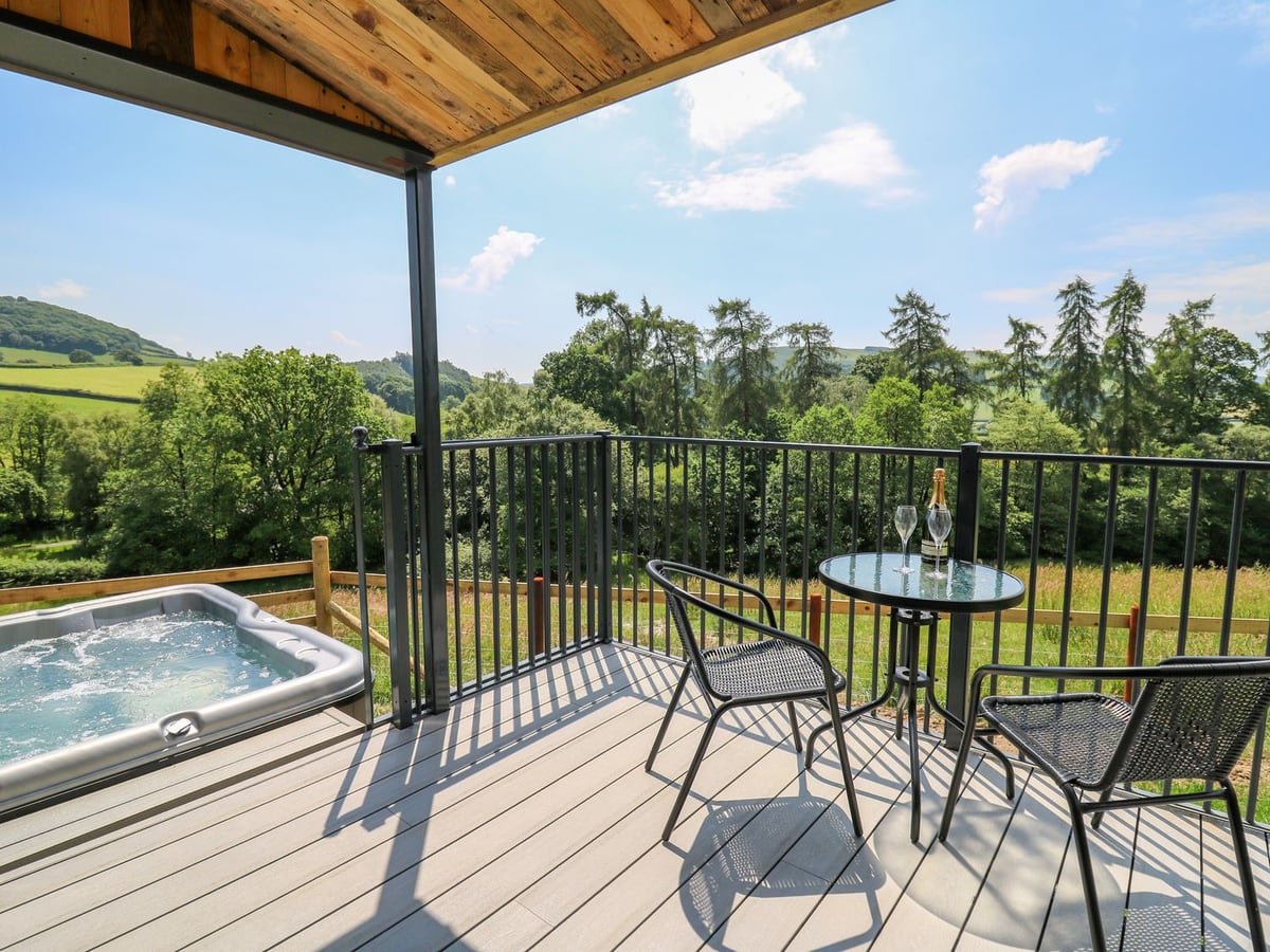 Hen's Hideaway railed deck with bistro table and chairs beside a hot tub, trees and fields beyond