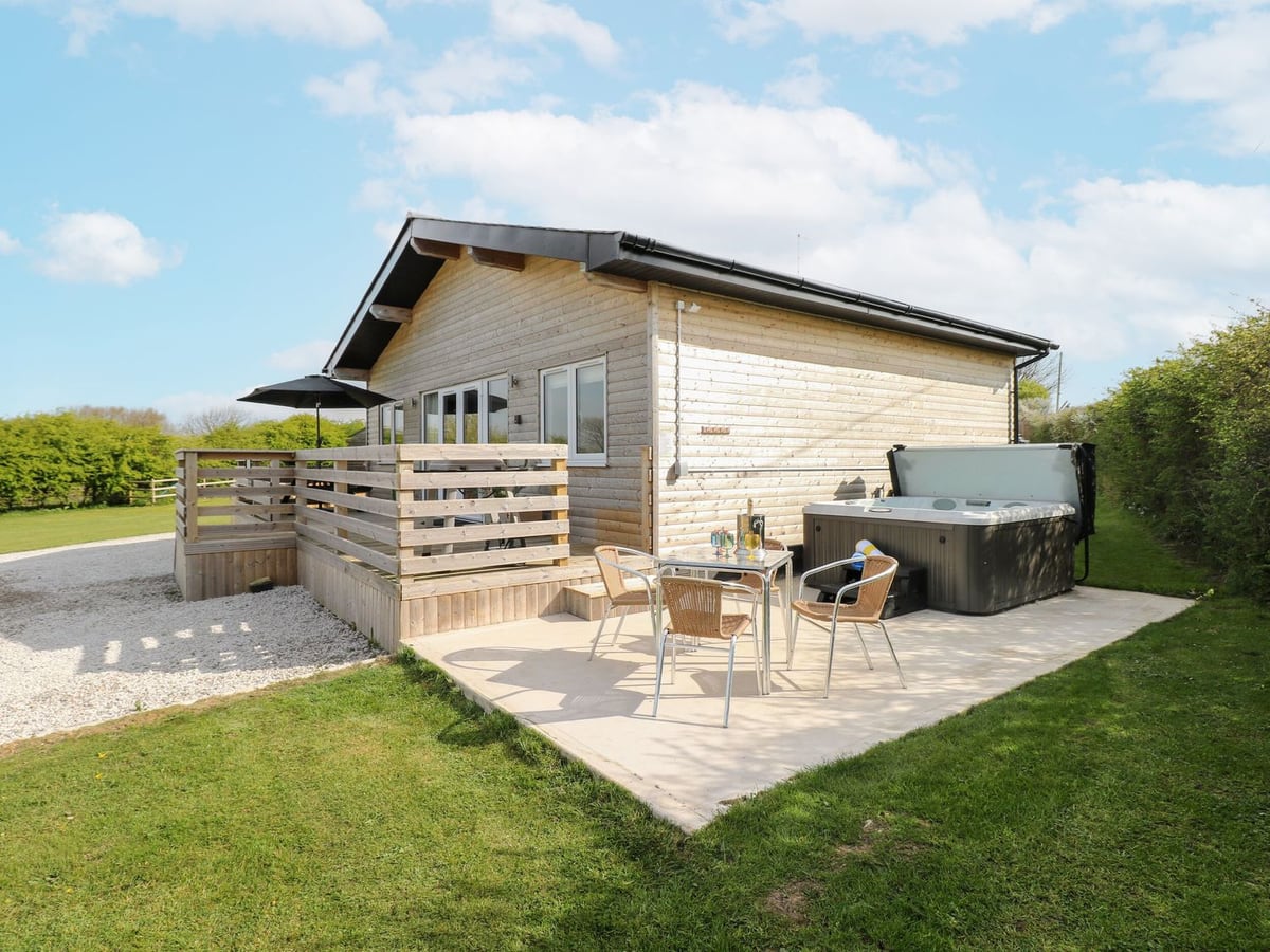 Heritage Retreat timber lodge with a patio table, chairs and hot tub beside a lawn and hedge