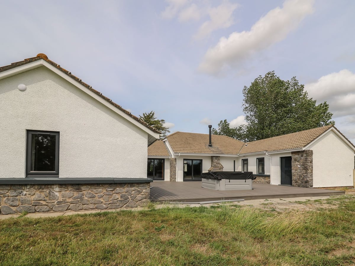 Heritage, a white single-storey house with stone details, decked courtyard, covered hot tub and grass