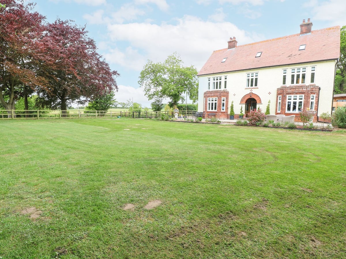 High House in Southrepps with a broad lawn, mature trees and a cream-coloured exterior