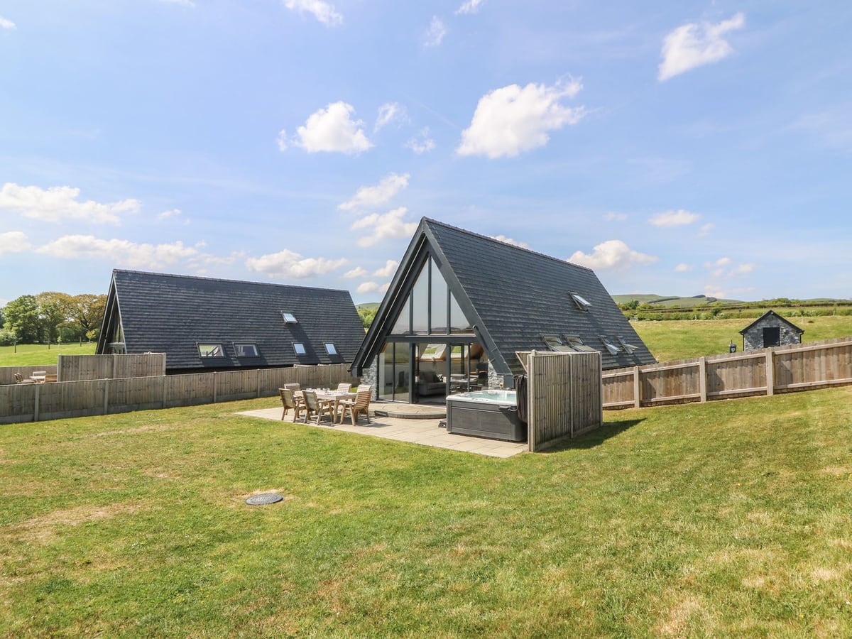 Hill Radnor A-frame lodge with patio dining, screened hot tub and fenced lawn, beside a similar lodge