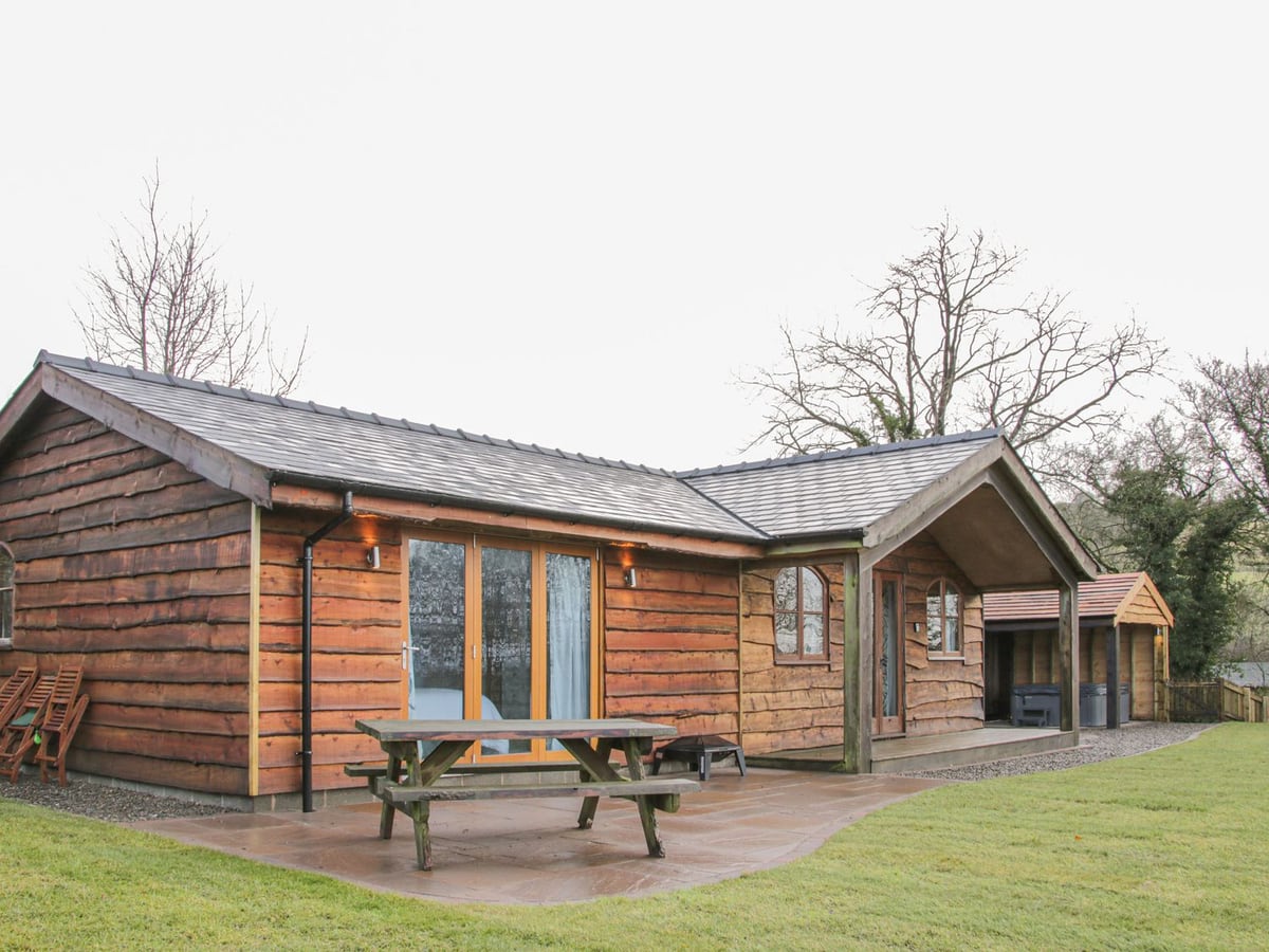 Hillside Lodge's timber exterior, picnic table and lawn, with a covered hot tub to the side