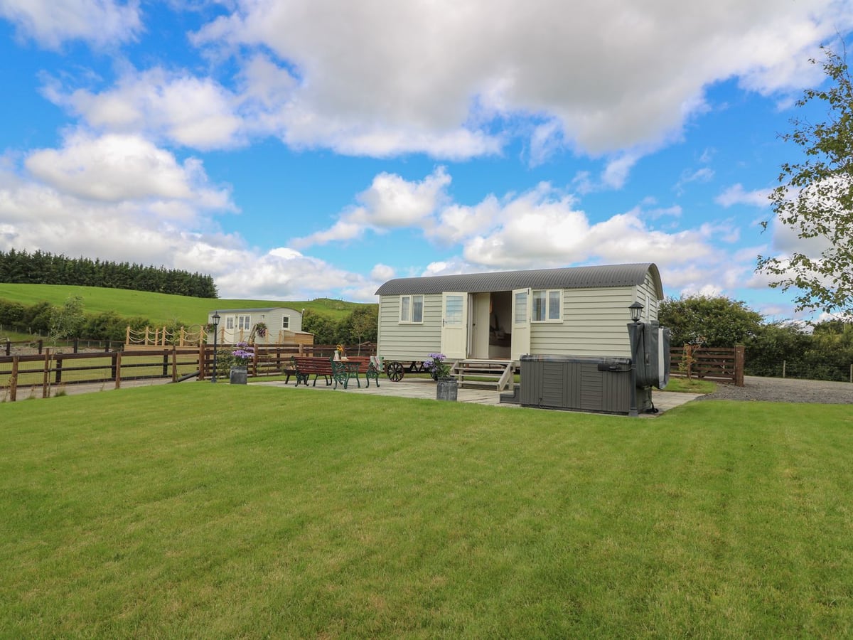 Hillside View shepherd's hut with patio, hot tub and benches beside a mown lawn and timber fencing