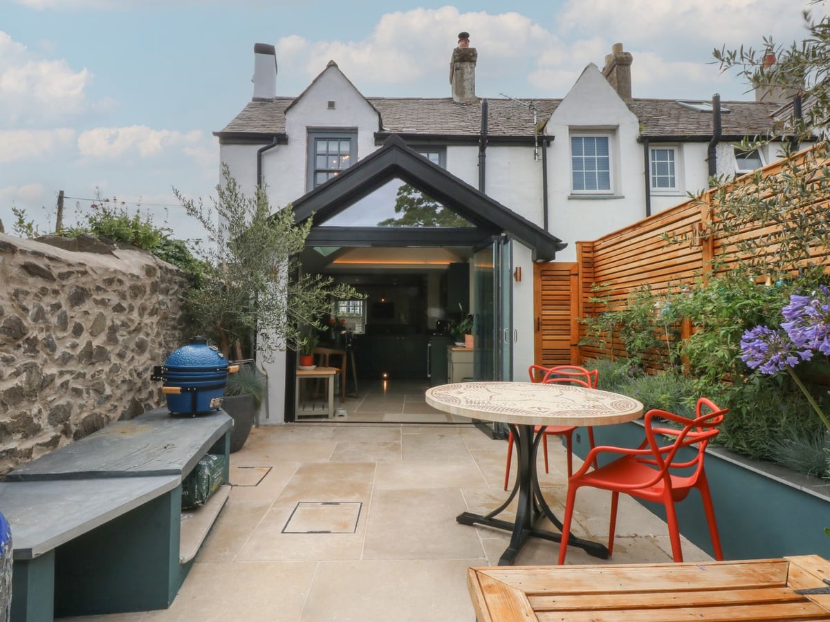 Hilltop Cottage paved courtyard with table, red chairs, planters and open glass doors to the house