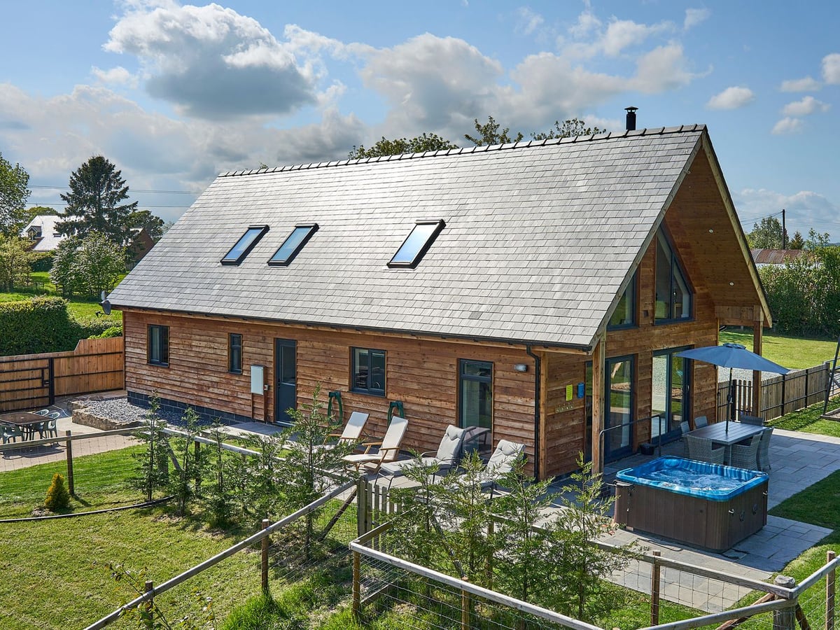 Holly Lodge timber house with a patio hot tub, loungers and lawn with post and wire fencing