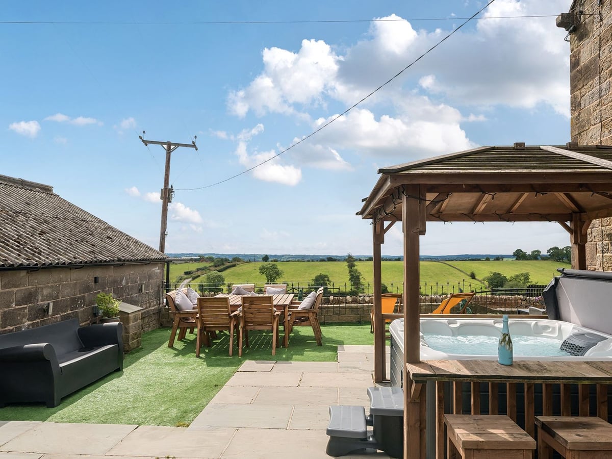 Hot tub under a wooden gazebo beside an outdoor dining table and fields at HollyDale.