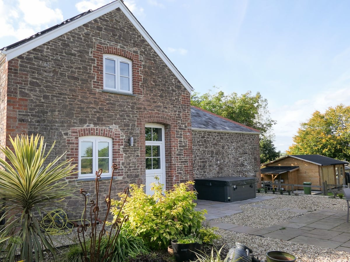 Stone gable and white windows beside a gravel courtyard and hot tub at Hope House Stables