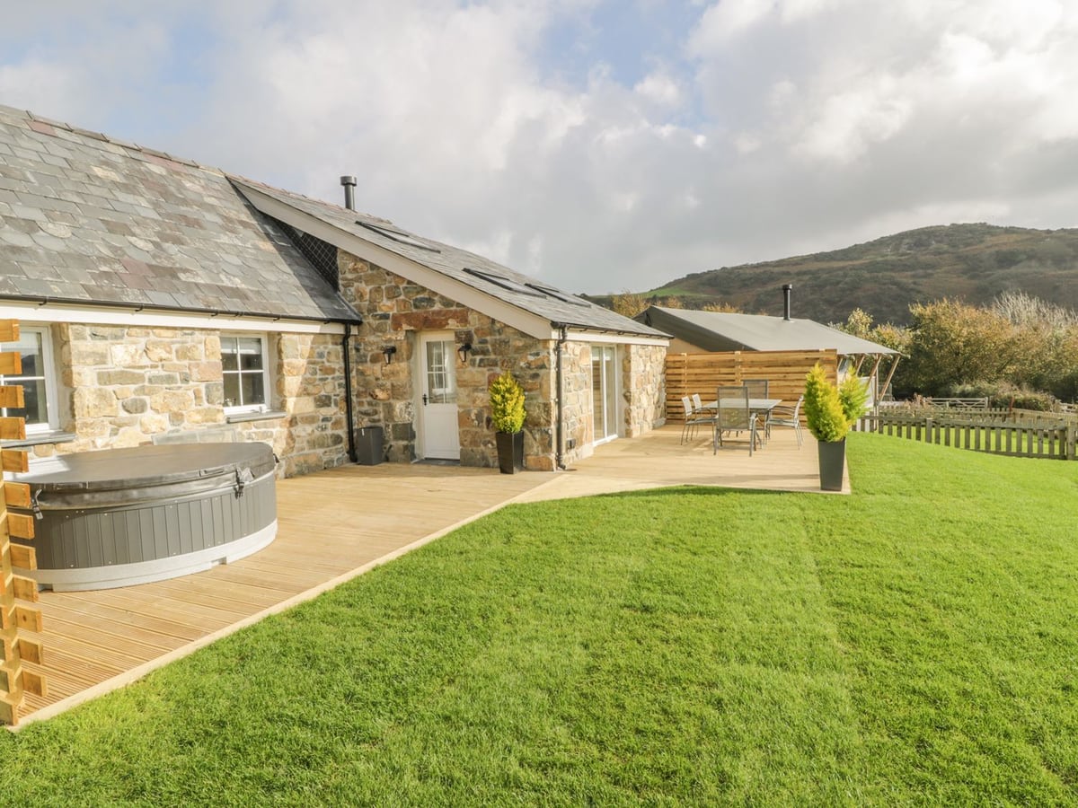 Hot tub with its lid on beside Horseshoe Cottage, with a lawn, dining set and hills behind