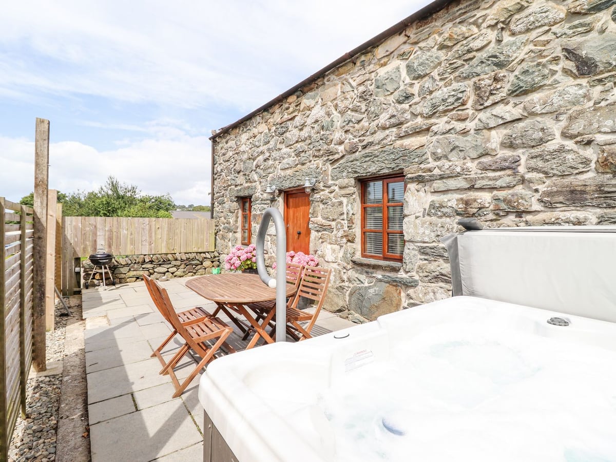 Isallt stone cottage with a fenced flagstone patio, wooden dining set, BBQ and hot tub with its lid raised