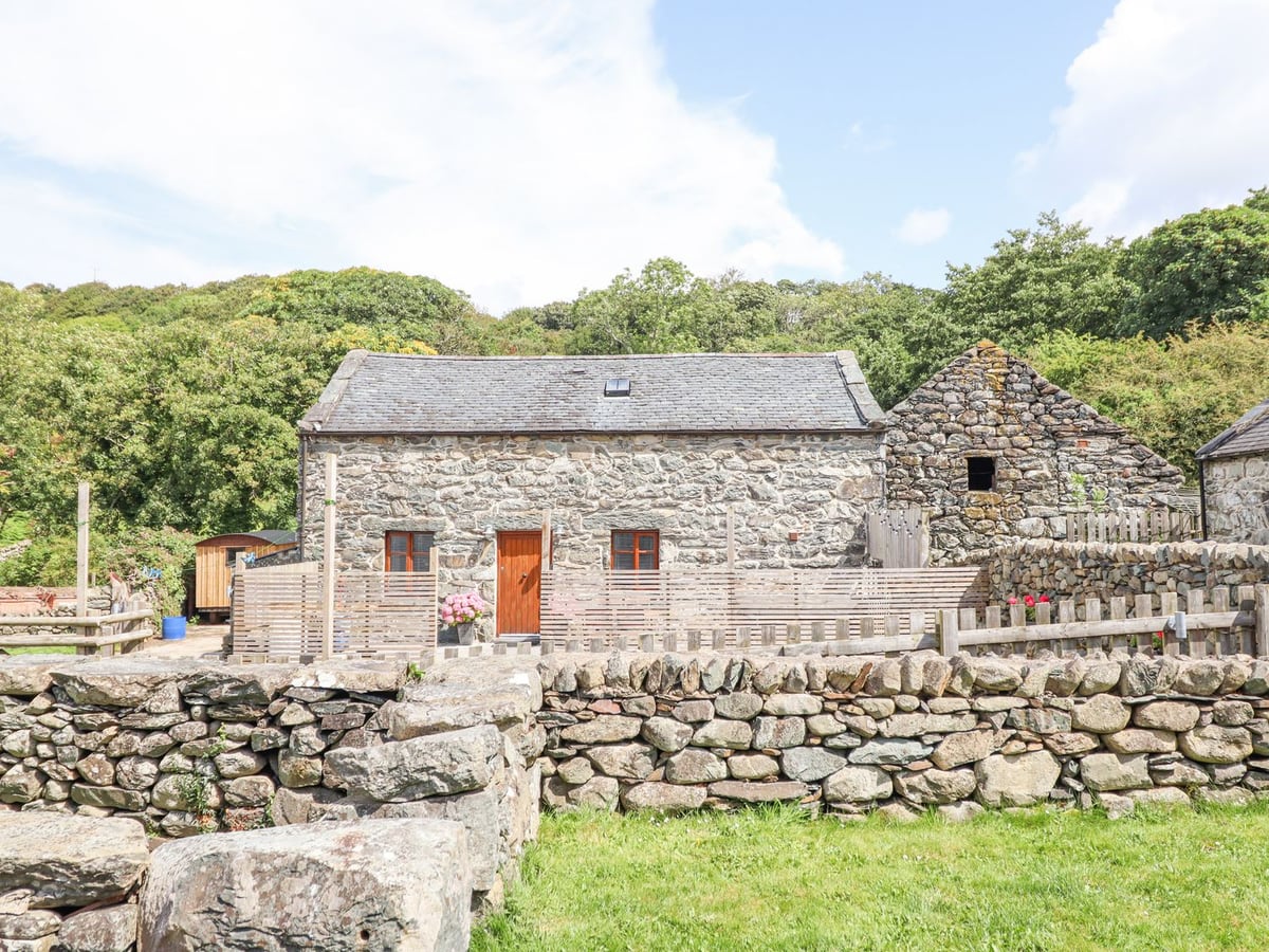 Isallt stone cottage exterior with fenced front courtyard, stone wall, and trees
