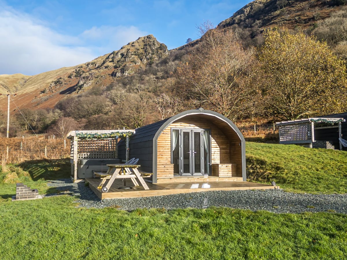 Jenny timber glamping pod with a picnic table and hot tub on the deck beneath a rocky hillside