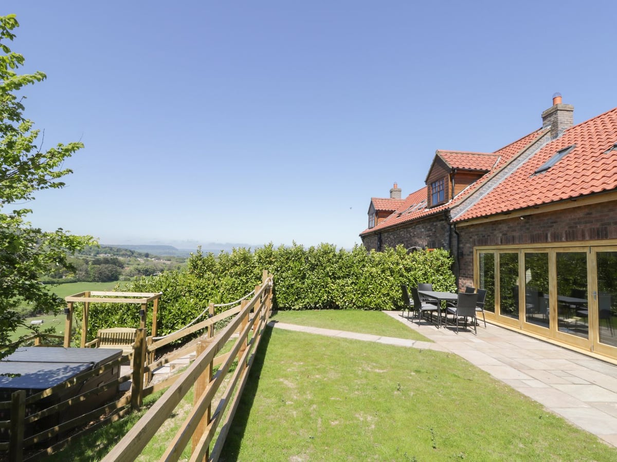 Lawn and paved terrace beside Kaitkyella Lodge, with timber rails and green hills beyond