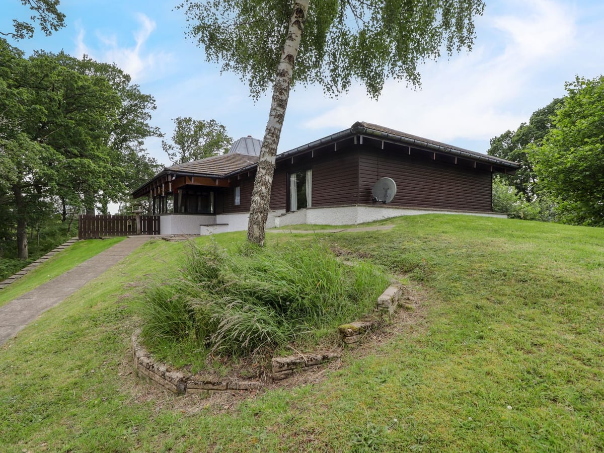 Katchana timber-clad house on a grassy bank, with outdoor seating and trees around the terrace