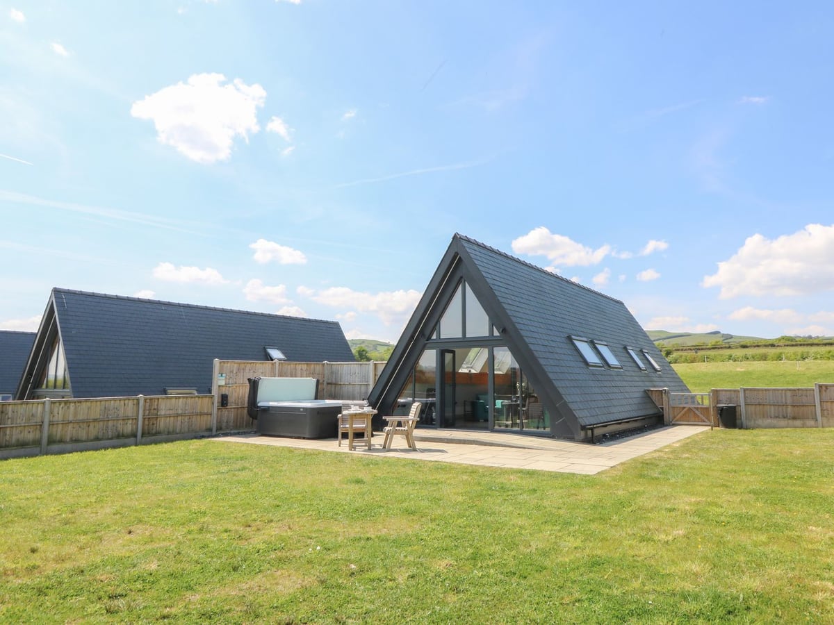 Kerry Hill A-frame lodge with lawn, patio seating, hot tub and fence beside a neighbouring lodge
